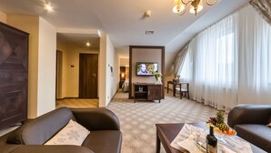 A modern living room with a sofa, a coffee table with a bottle and glasses, a TV, and a dining area with a fruit bowl. - Hotel Ostaniec (Kroczyce)