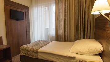 Habitación de hotel con cama, televisor montado en la pared, lámpara de noche y teléfono en la mesita de noche.