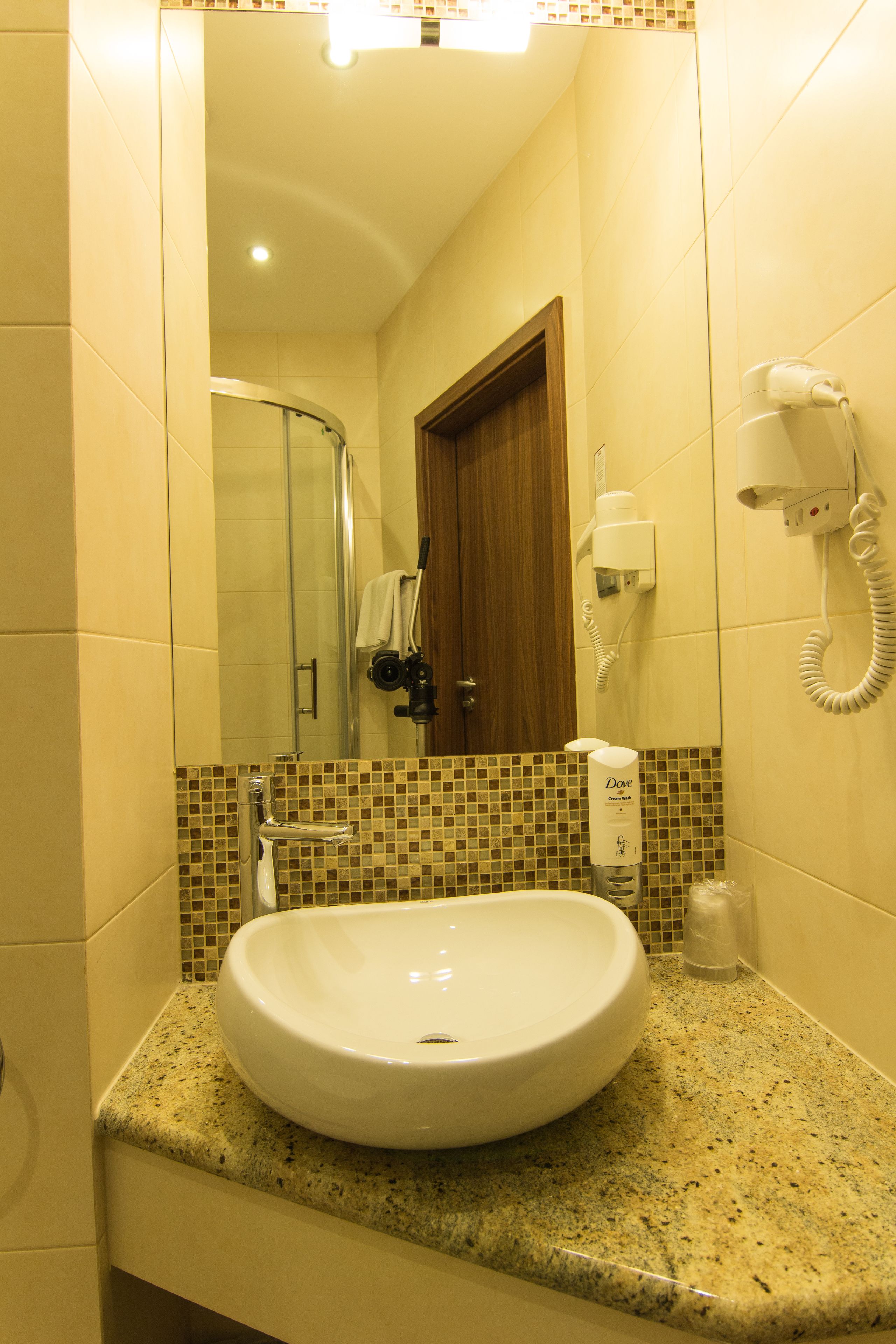 A bathroom with a sink, mirror, shower, and hairdryer.
