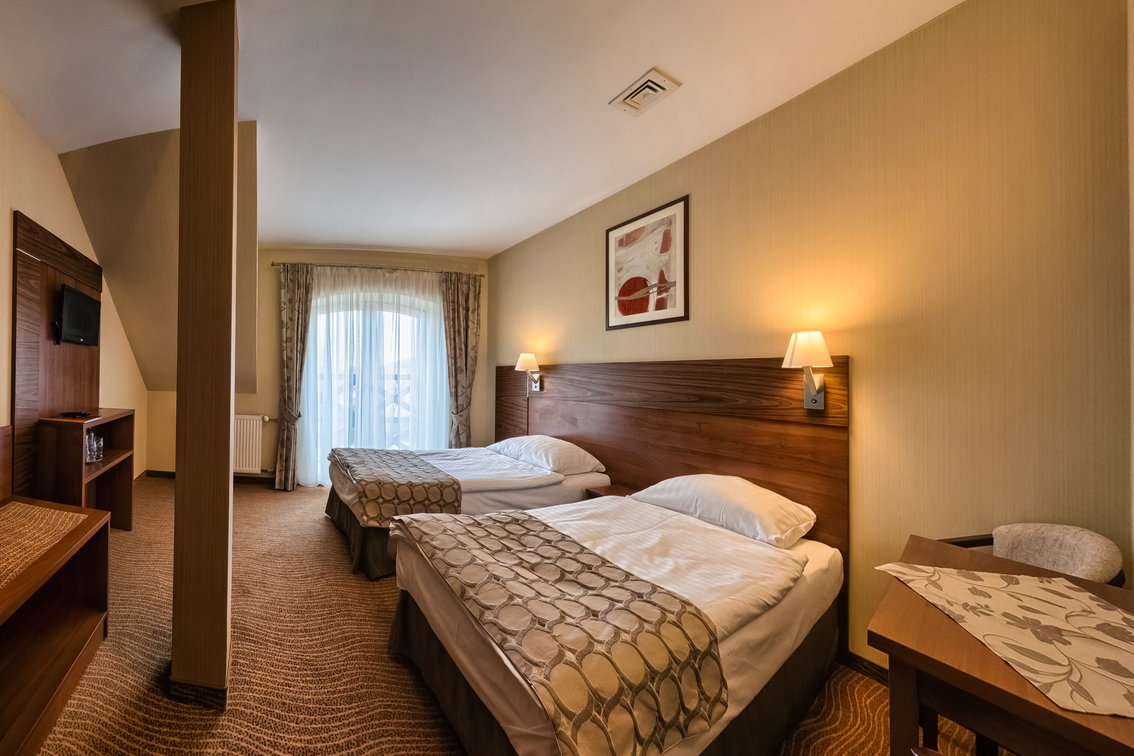 Habitación de hotel con dos camas, televisión, escritorio y ventana con cortinas.