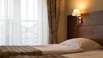 Una habitación de hotel con una cama, una mesita de noche con lámpara y una ventana con cortinas traslúcidas.
