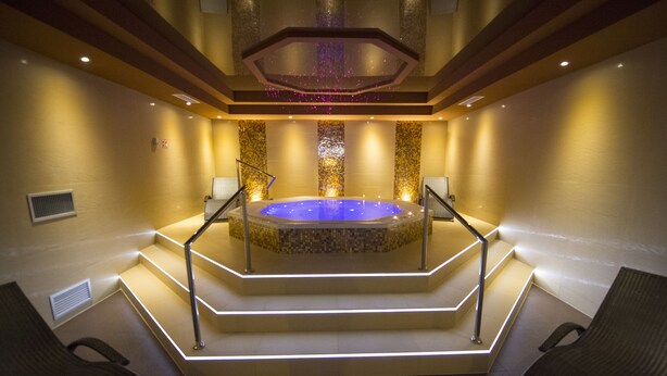 A spa area with a hot tub, steps leading to it, and two chairs. - Hotel Ostaniec (Kroczyce)