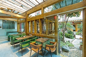 Un restaurante con vigas de madera, asientos verdes y vistas a un jardín.