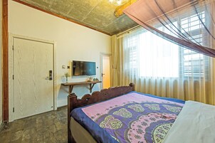 Un dormitorio con cama, televisor en la pared, una puerta y una ventana con cortinas.