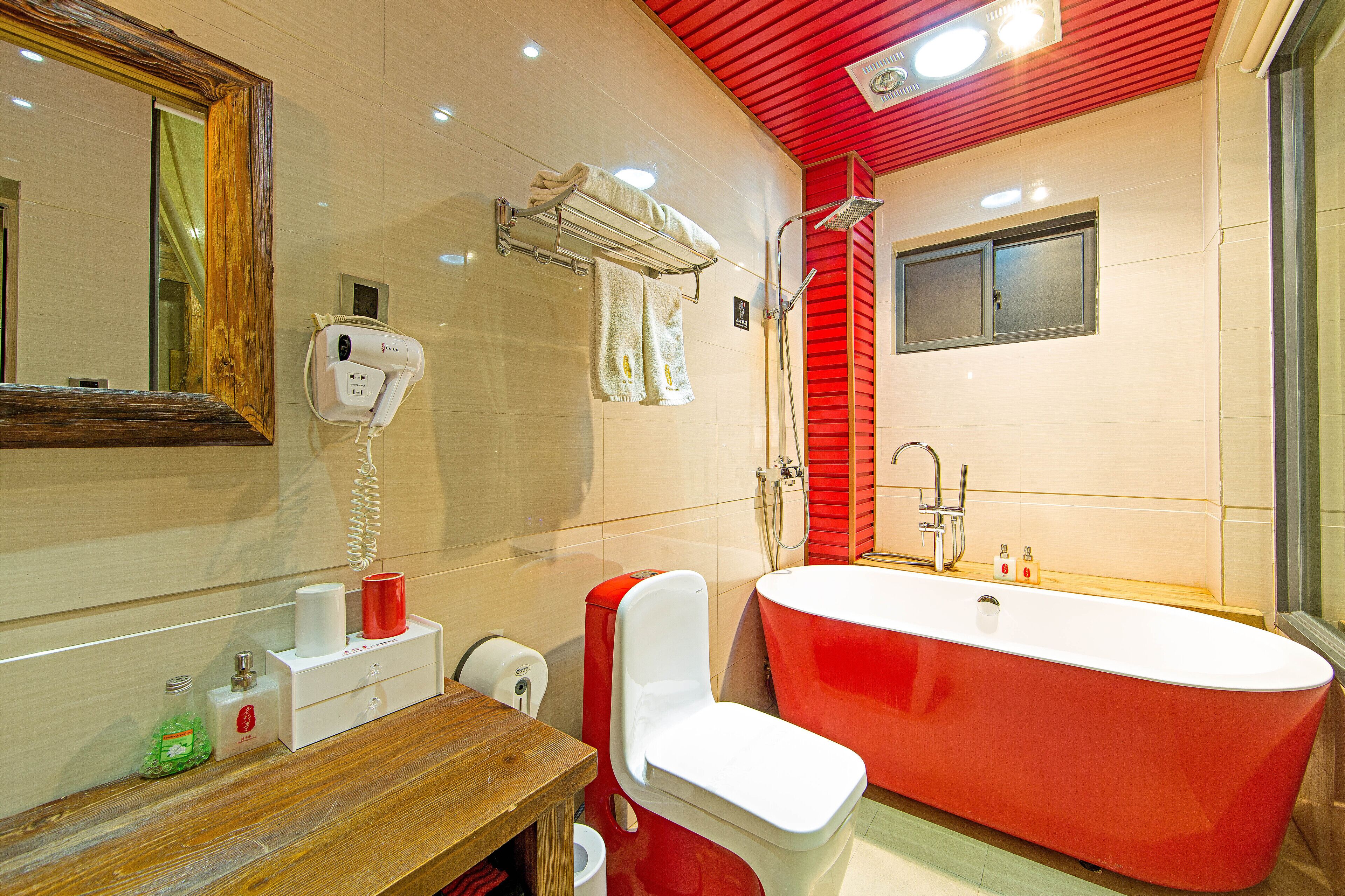 A modern bathroom with a red bathtub, a white toilet, and a mirror with a wooden frame.