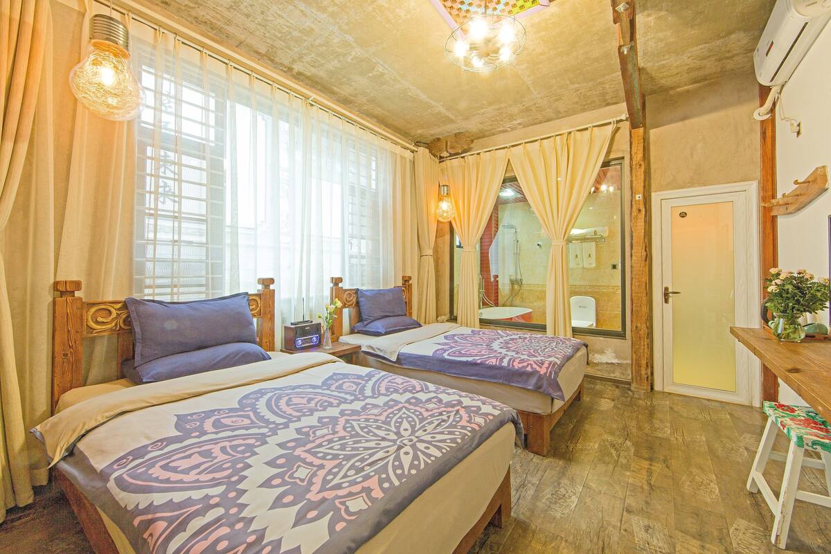 A room with two beds, a wooden headboard, a desk with a chair, a mirror, and a door.