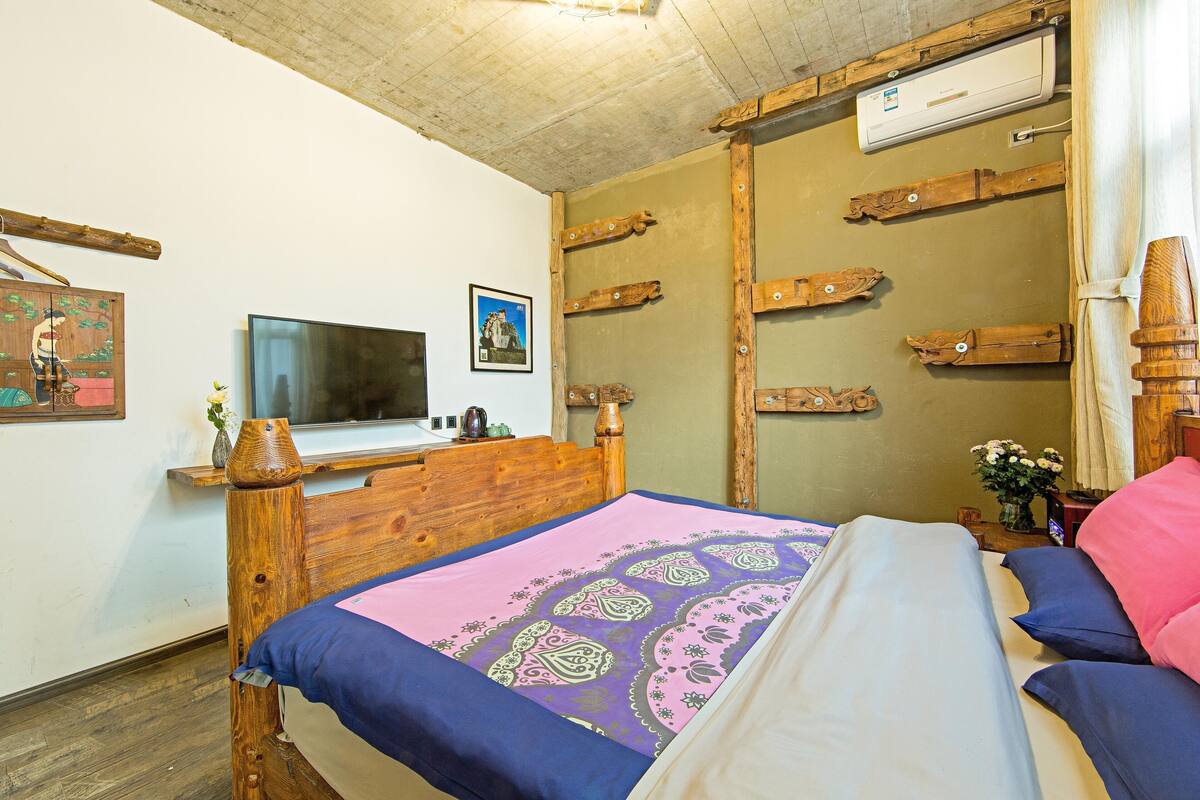 A bedroom with a wooden bed, a television, a wooden wardrobe, and a small table with a vase.