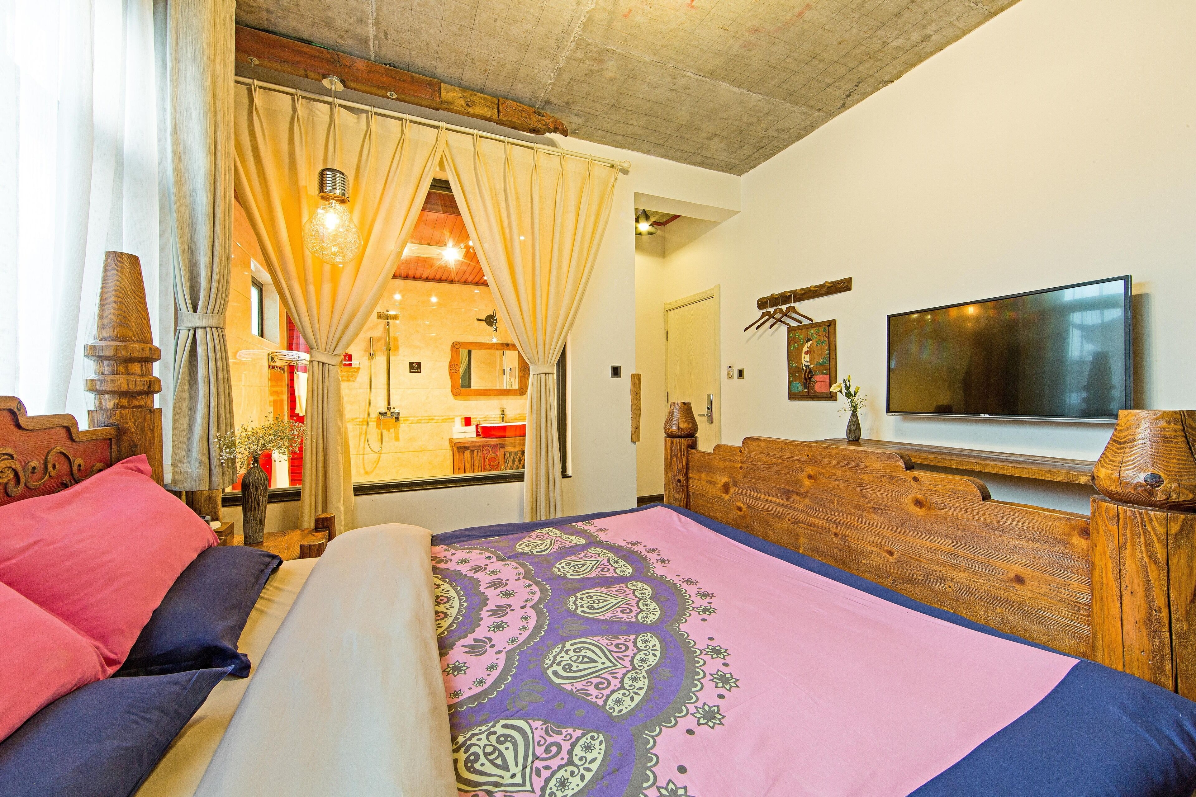 A bedroom with a bed, curtains, a television, and a bathroom visible through an open door.