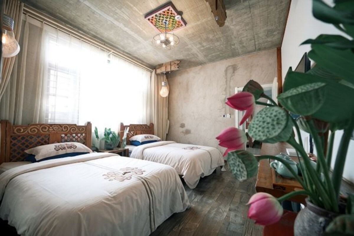 A room with two beds, a wooden headboard, a large window, and a plant.