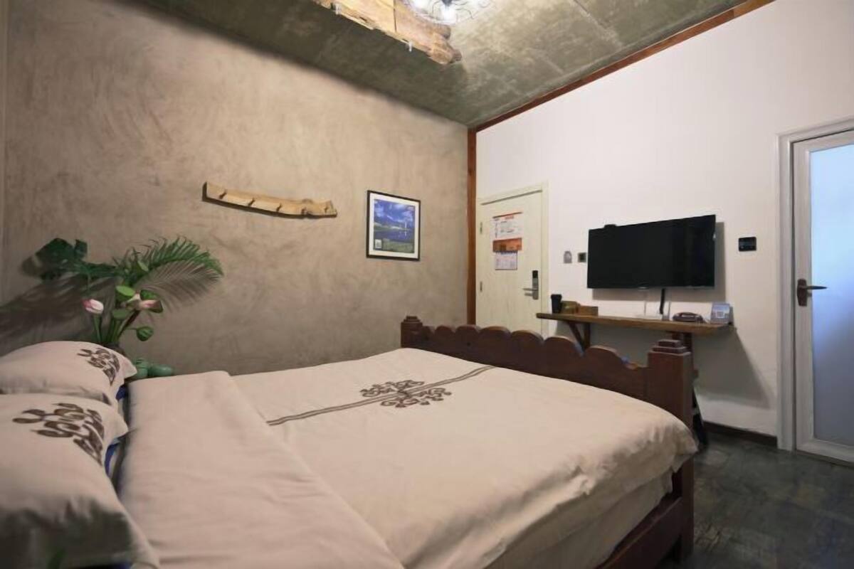 A bedroom with a bed, a television on a stand, a wooden shelf, a framed picture, and a door.