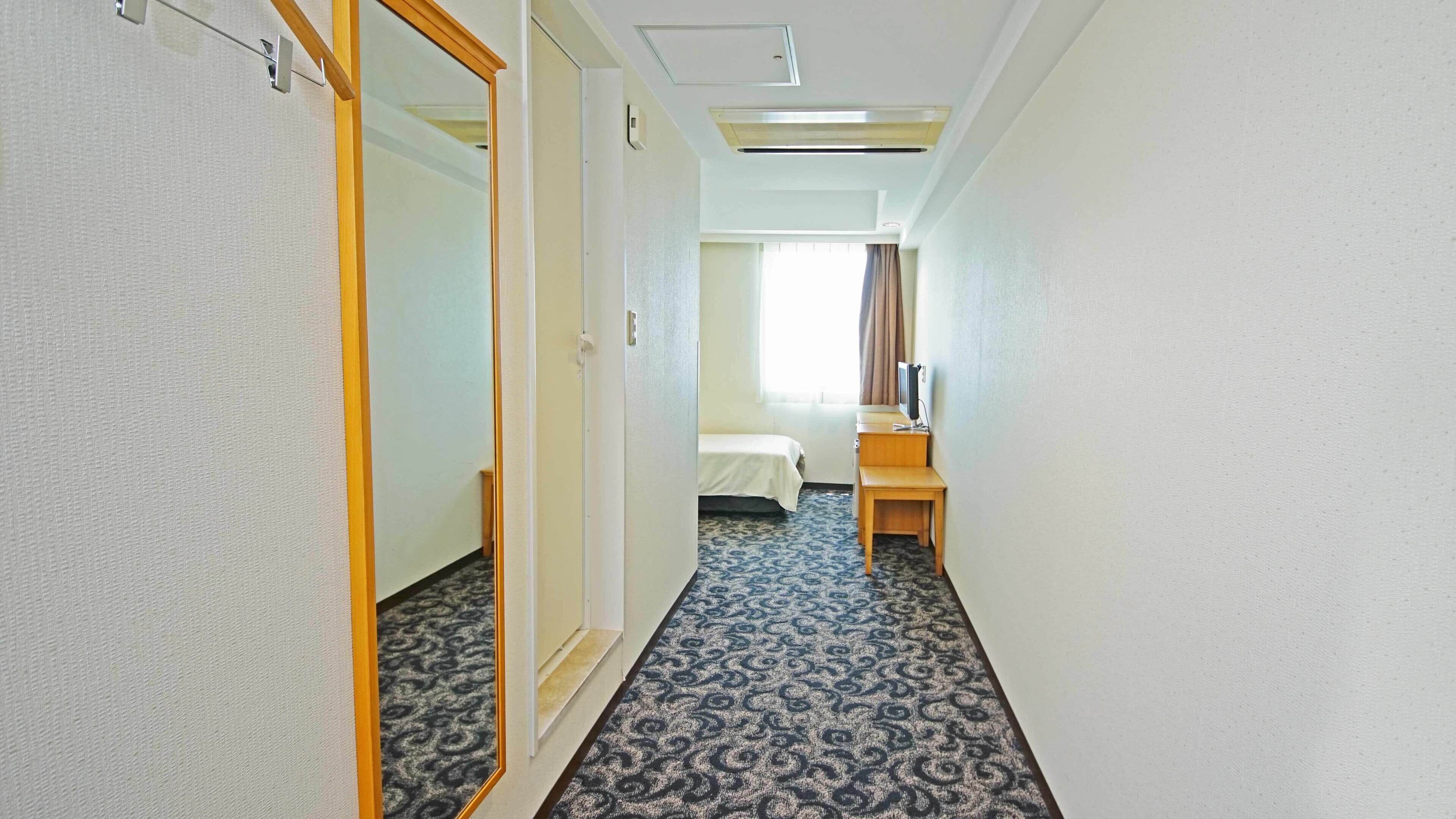 A hotel hallway with a bed, a desk, and a mirror.