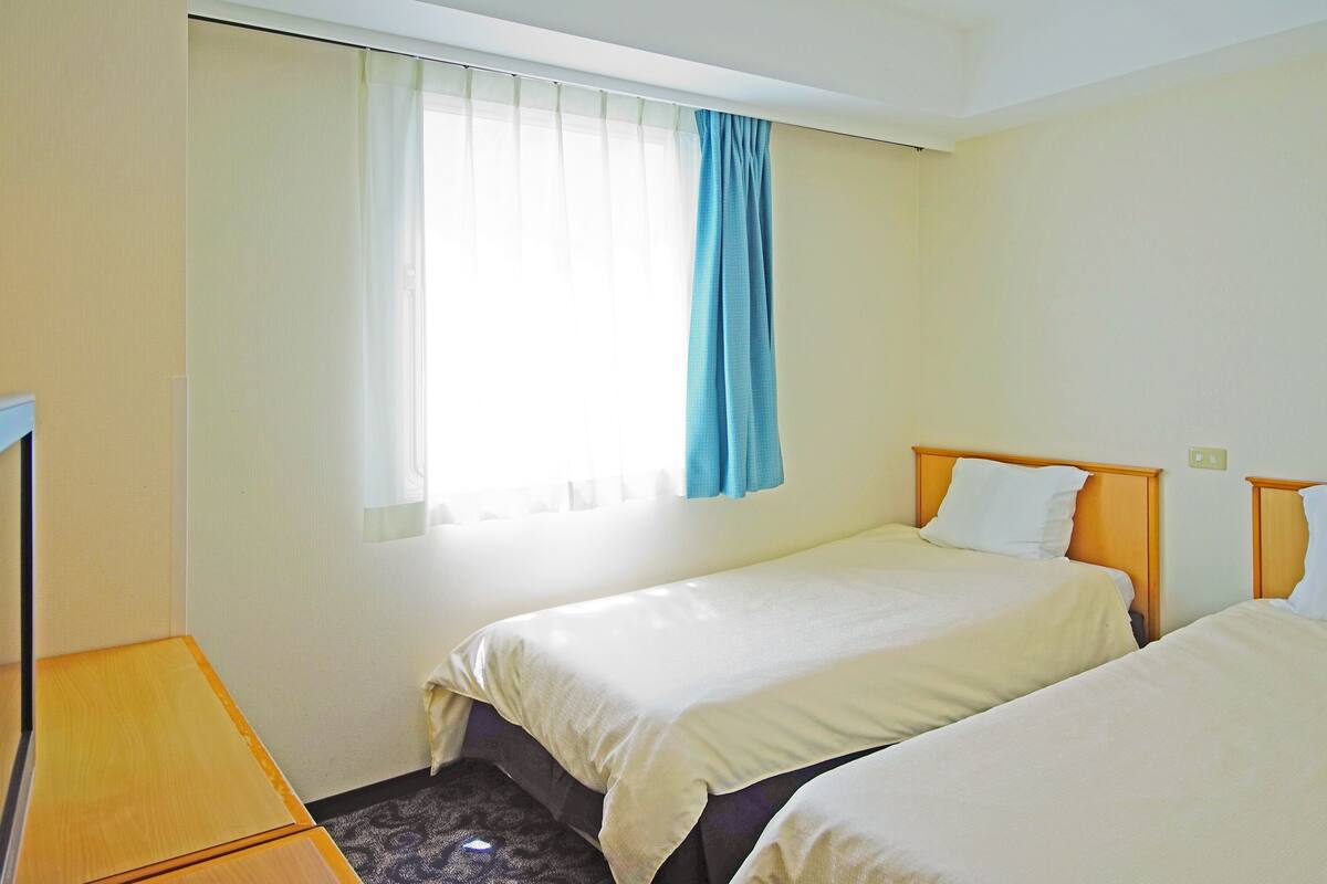 A hotel room with two beds, a window with curtains, and a desk.