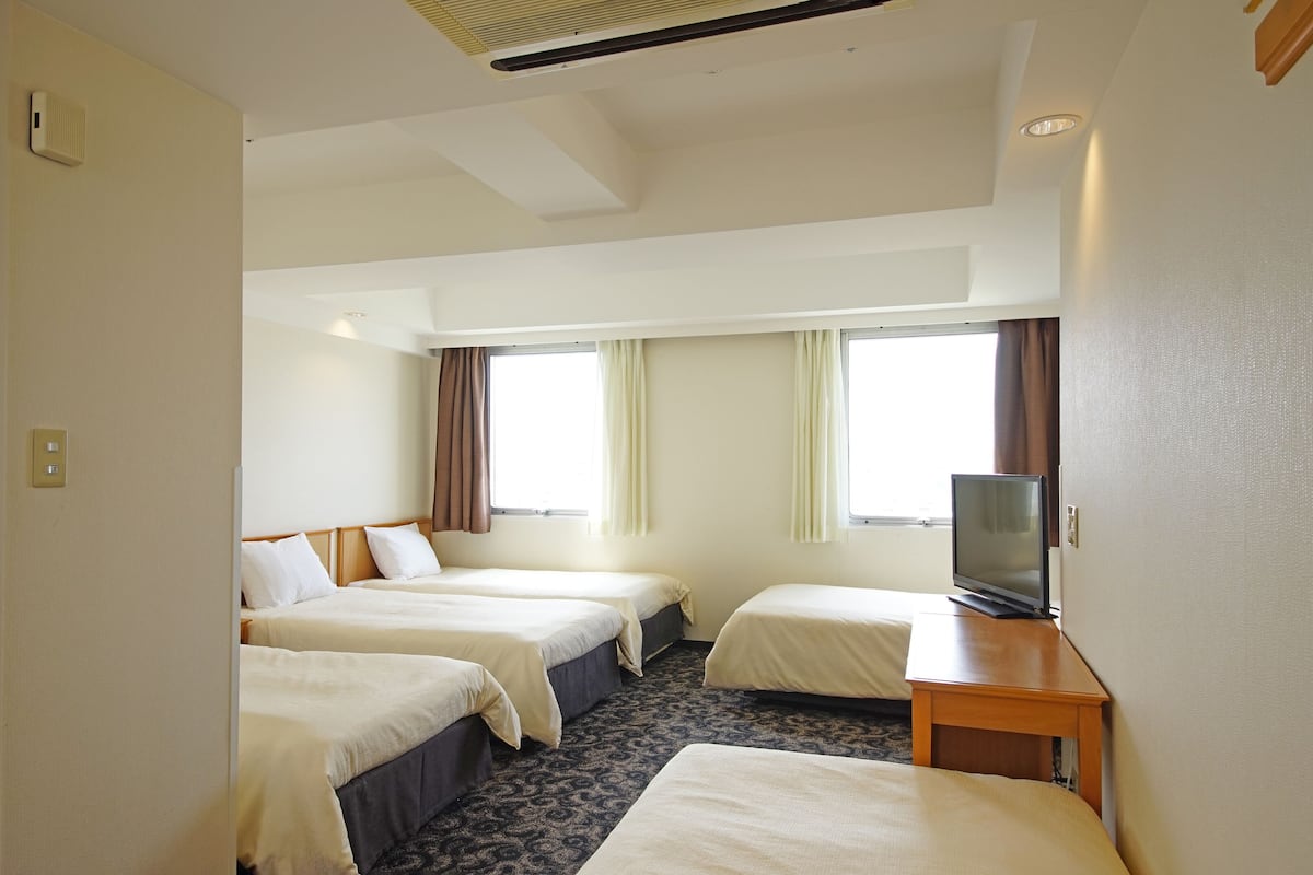 A hotel room with two beds, a TV, and a window with curtains.