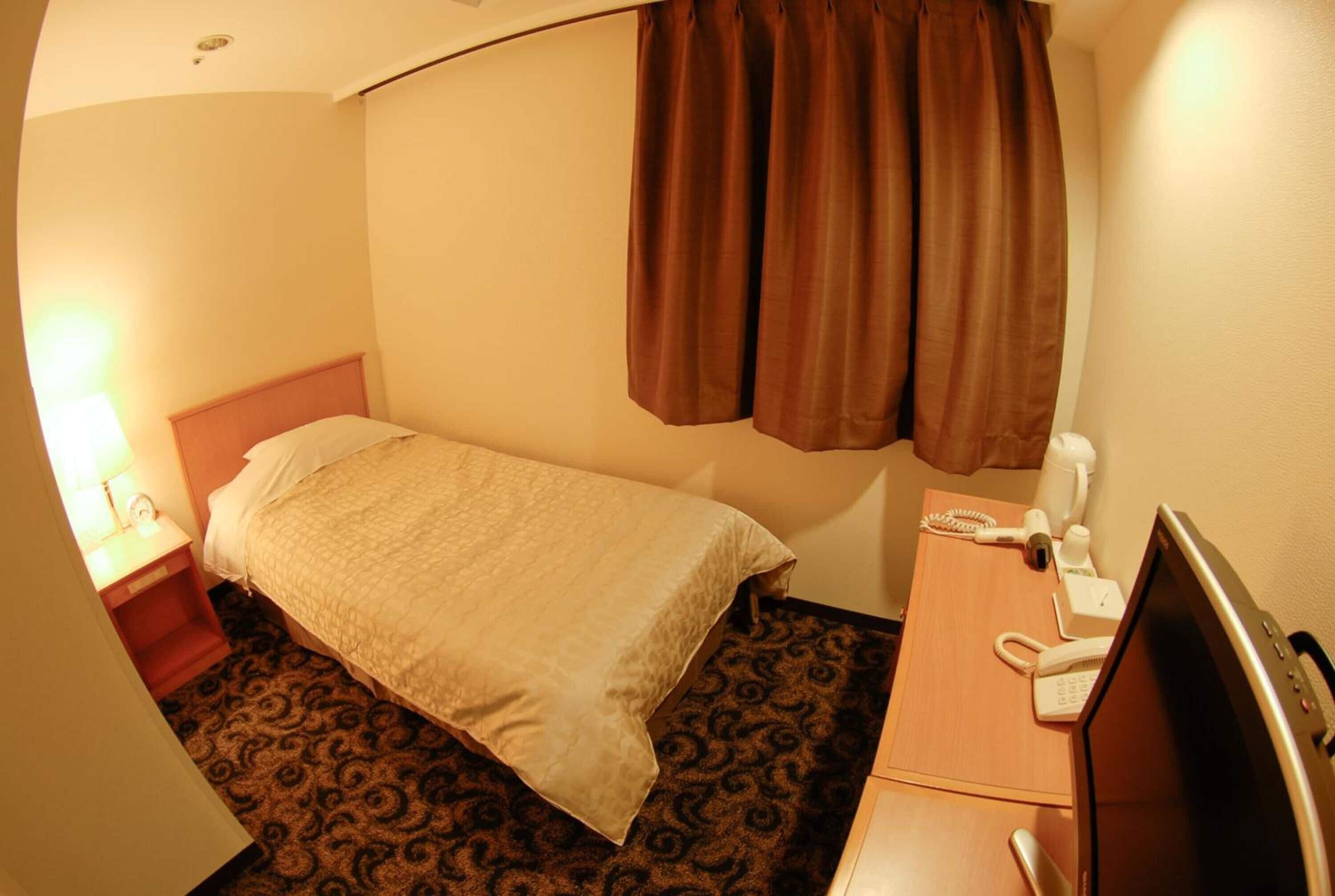 Een hotelkamer met een bed, een bureau met telefoon en een televisie.