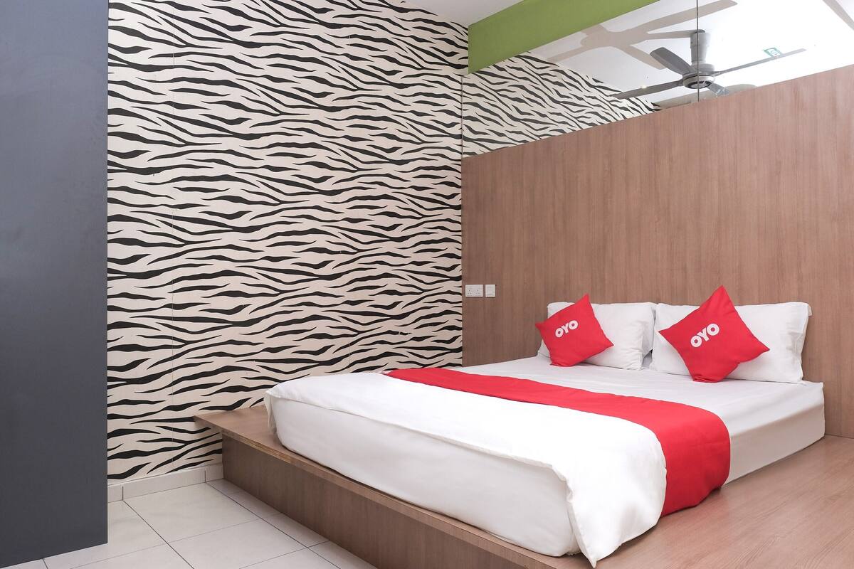 A modern hotel room with a zebra-patterned wall, a wooden headboard, a bed with white bedding and red accents, and a ceiling fan.