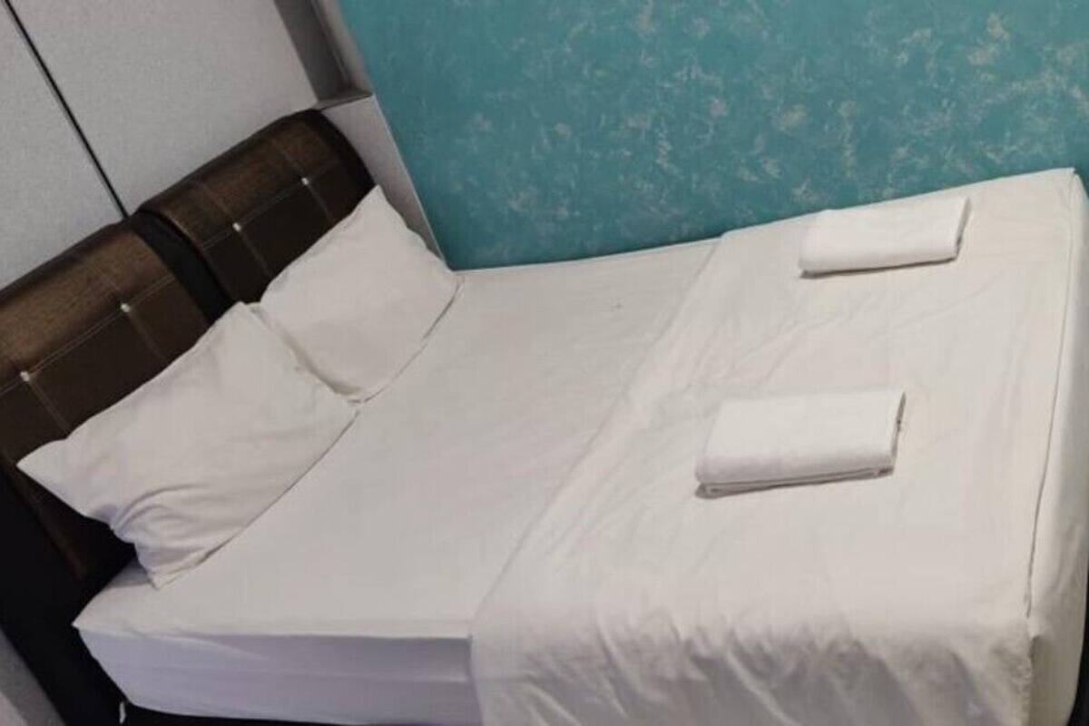 A neatly made bed with white linens and two folded towels on the side.