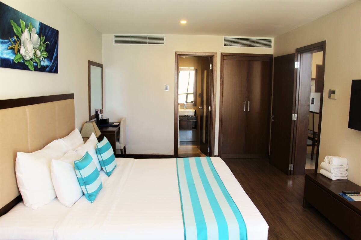 A hotel room with a large bed, a desk, a mirror, a TV, and a wardrobe.