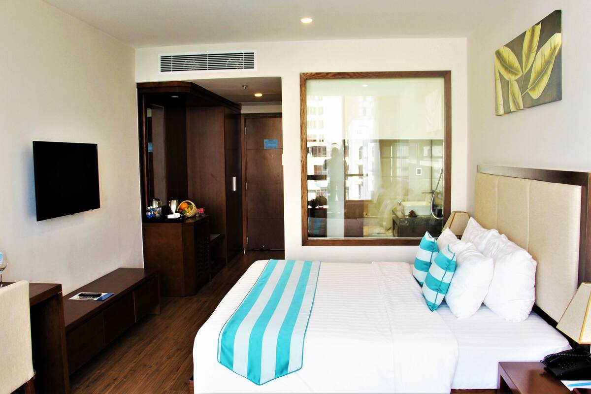 A hotel room with a bed, a TV, a desk, a window with a view, and a door leading to a bathroom.