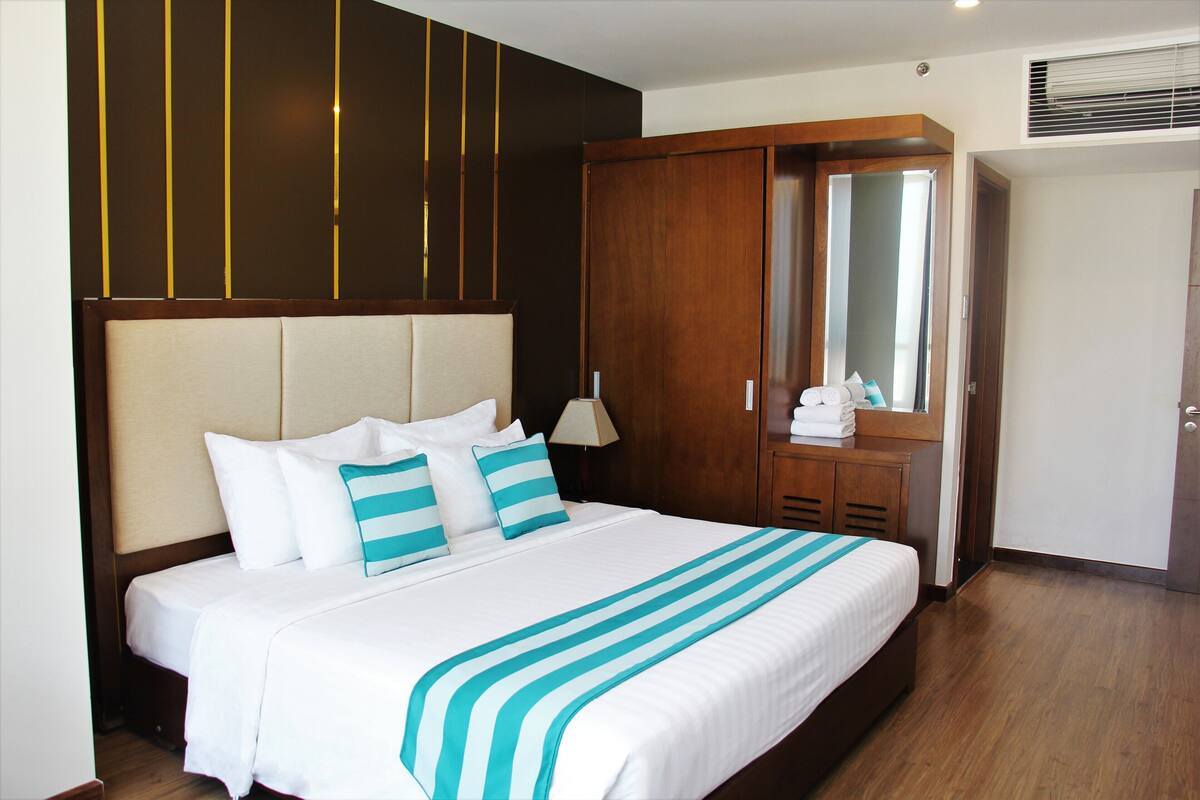 A neatly made bed with white and teal bedding, a wooden headboard, and a large mirror above it.