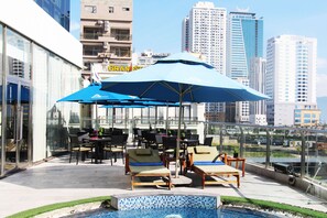 A rooftop pool area with lounge chairs and umbrellas, surrounded by high-rise buildings.