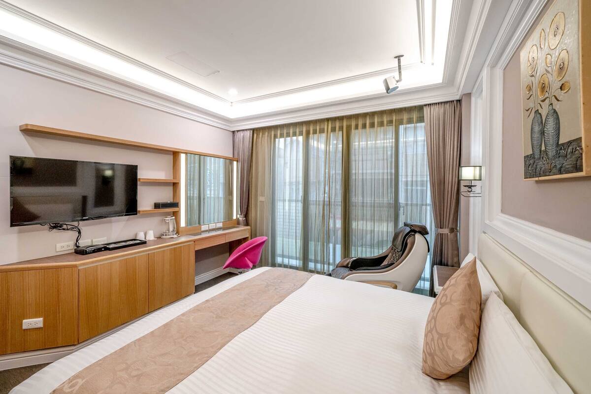 Habitación de hotel con una cama grande, un escritorio con televisor de pantalla plana, una silla y una ventana con cortinas.