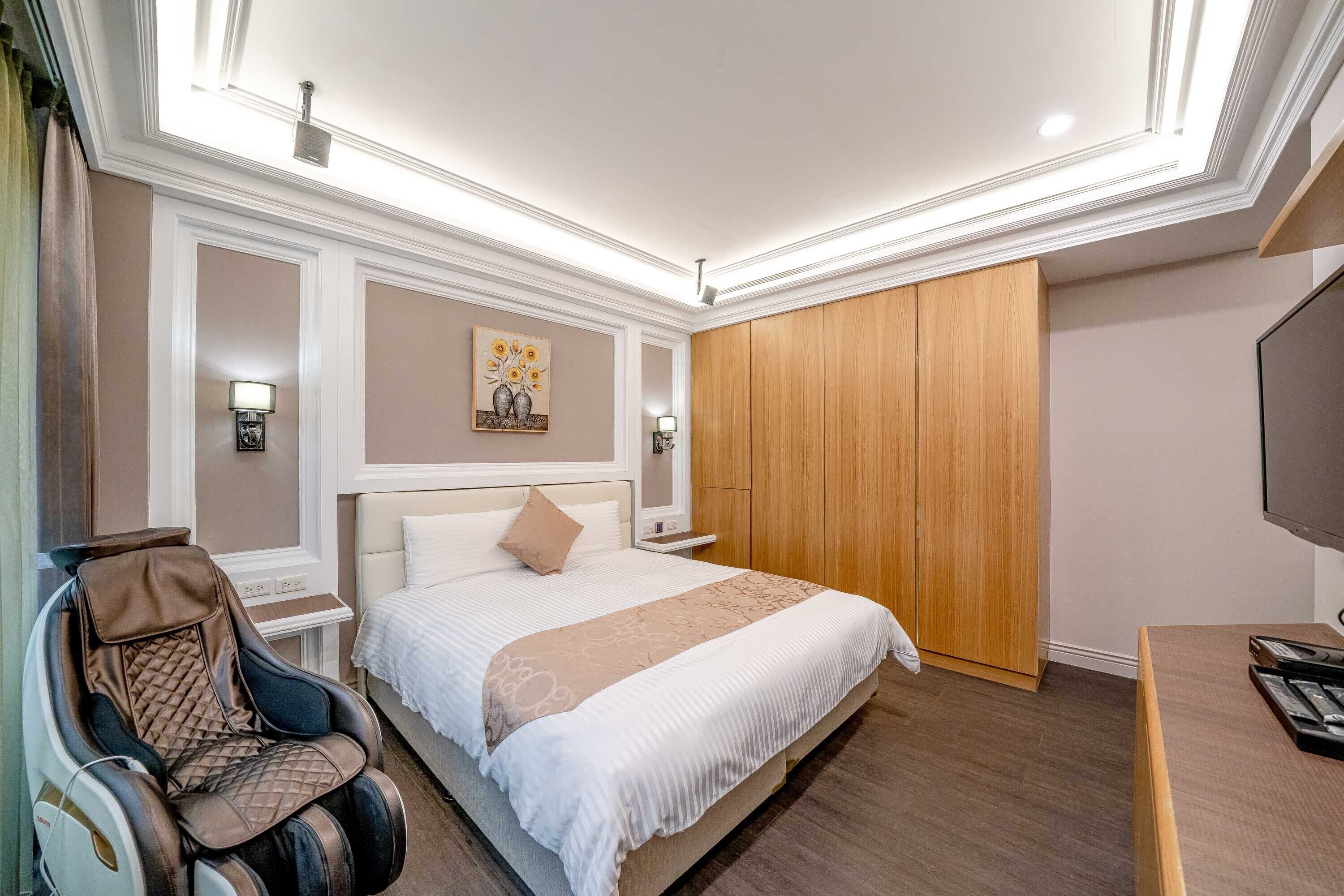 Une chambre d’hôtel équipée d’un lit, d’un fauteuil massant, d’une armoire en bois et d’un téléviseur.