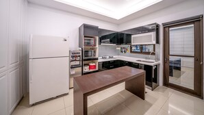 Een moderne keuken met een ingebouwde oven, magnetron en koelkast. Er staat een houten tafel en boven de gootsteen is een raam.