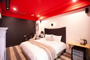Ein Hotelzimmer mit Bett, Nachttisch mit Lampe, kleinem Fernseher und roter Decke.