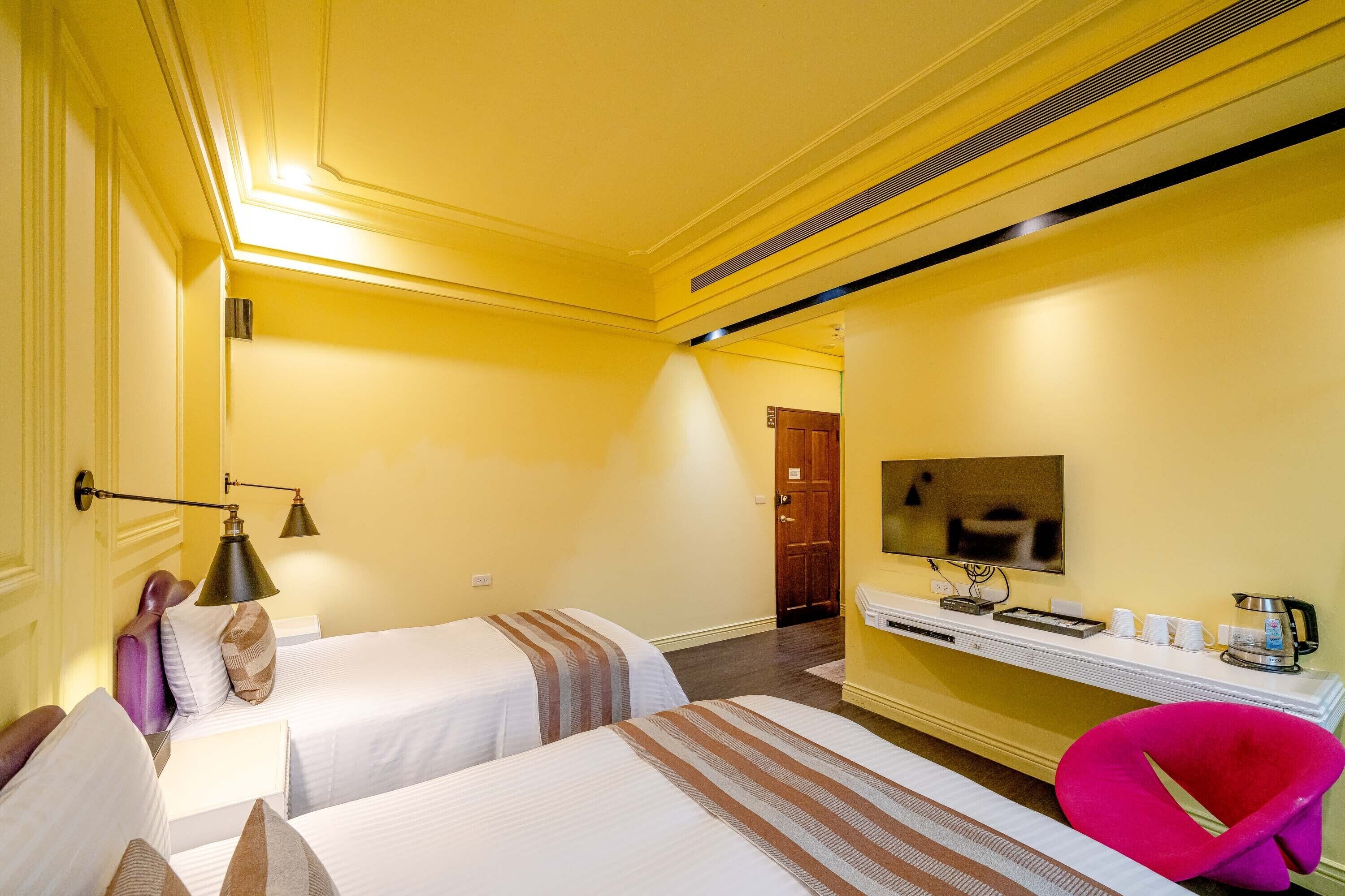 Habitación de hotel con dos camas, un escritorio, un televisor de pantalla plana, una cafetera y un esquema de color amarillo brillante.