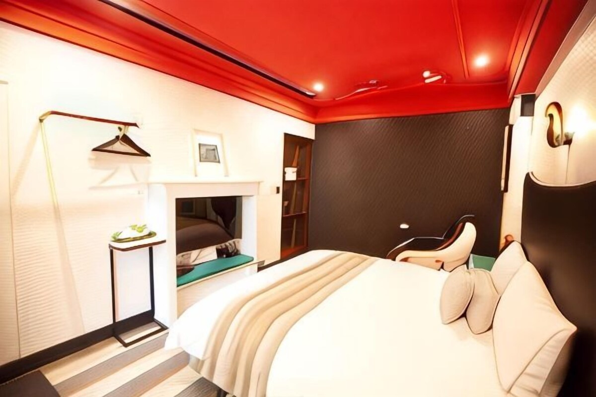 Una habitación de hotel moderna con una cama, una mesita de noche y un techo rojo.