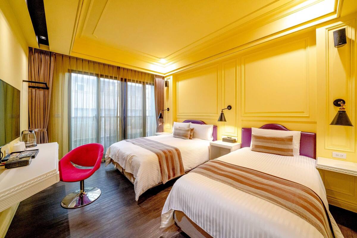 Habitación de hotel con dos camas, un escritorio, una silla y un televisor.