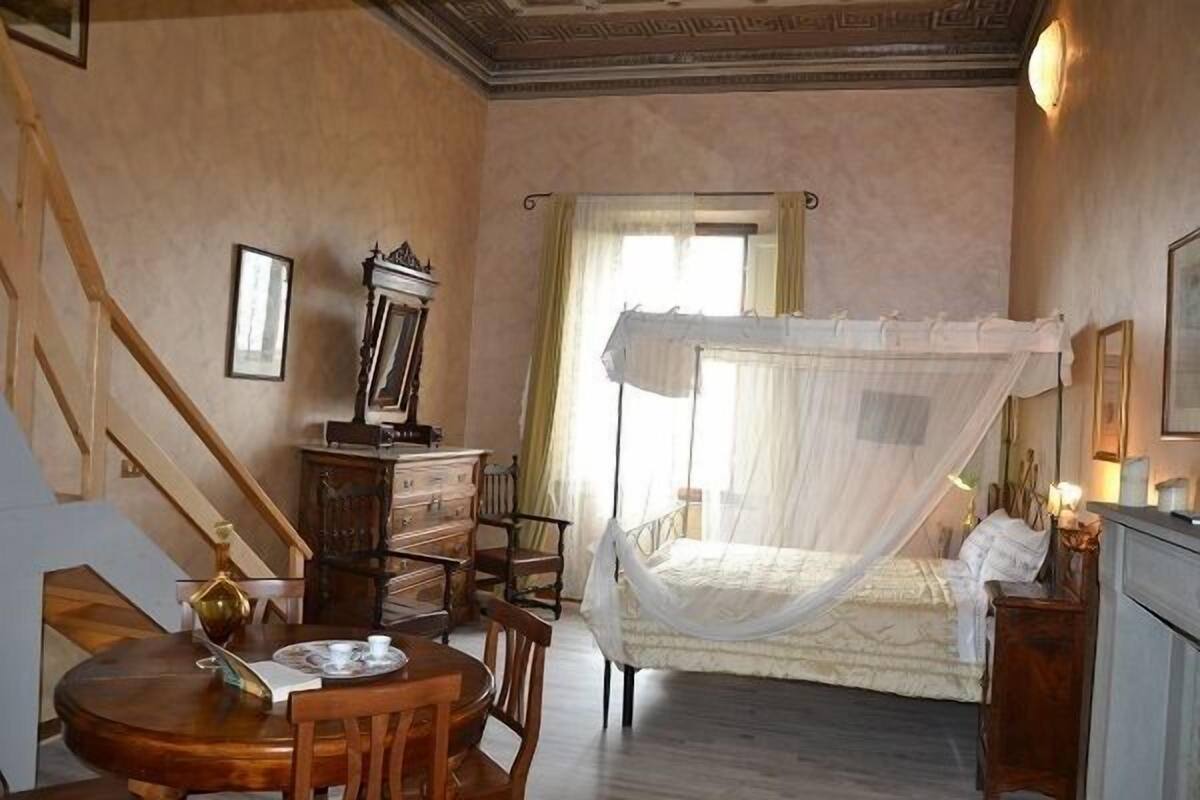 A bedroom with a bed, a wooden dresser, a desk with a chair, and a staircase.