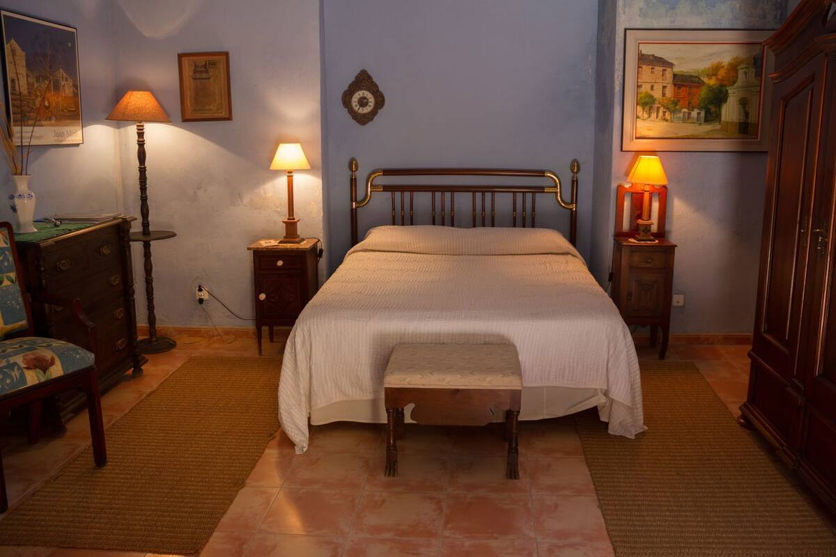 A bedroom with a bed, bedside tables, a chair, a dresser, and wall-mounted lamps.
