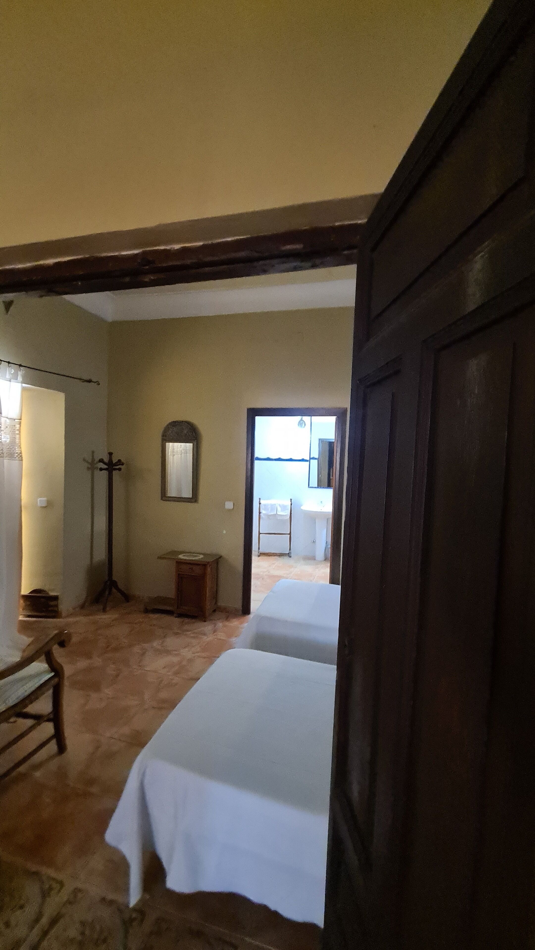 A room with a bed, a wooden bench, a coat rack, and a door leading to a bathroom.