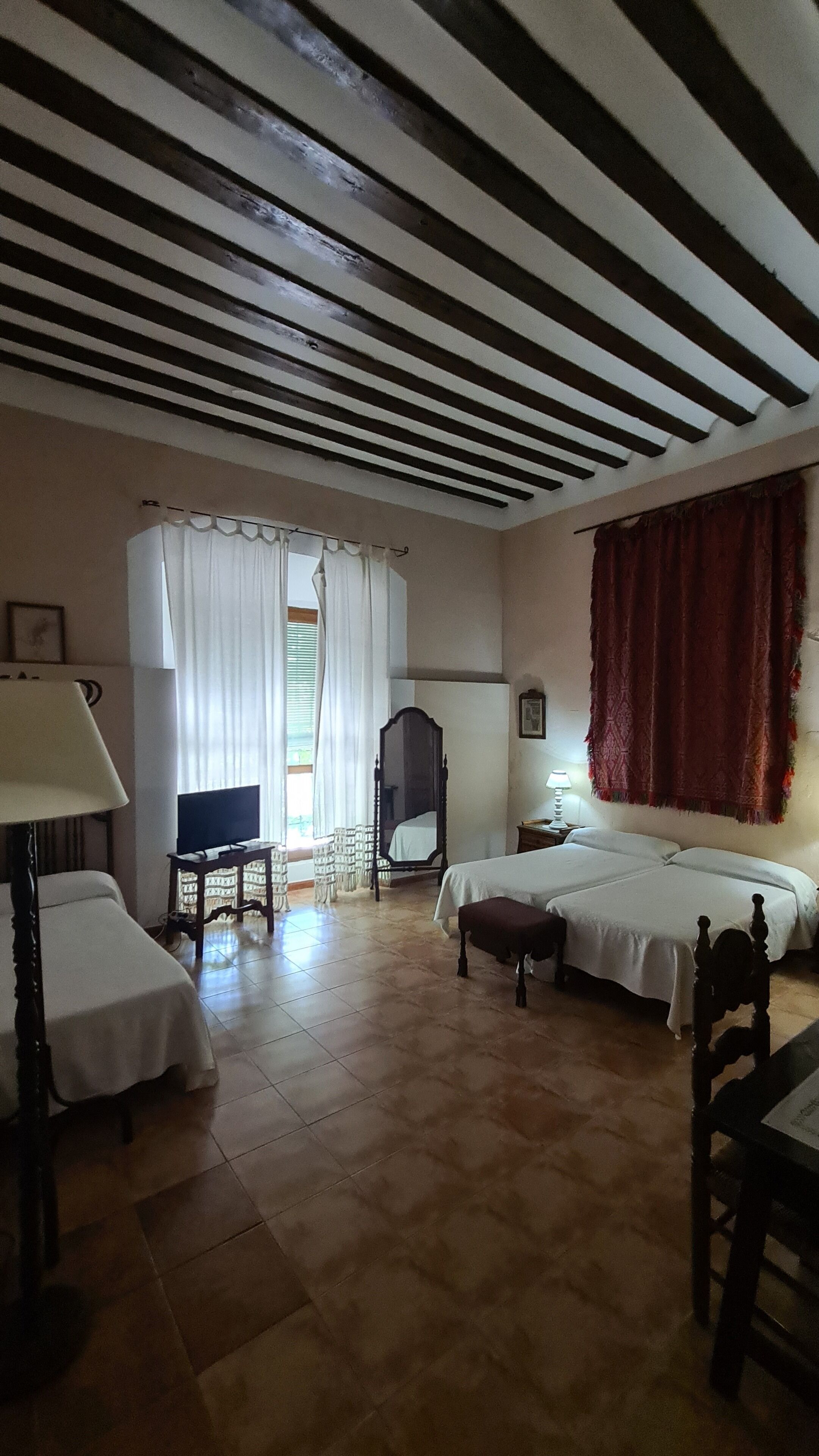 Ein Hotelzimmer mit zwei Betten, einem Fernseher, einem Schreibtisch, einem Stuhl, einem Spiegel und einem Fenster mit Vorhängen.