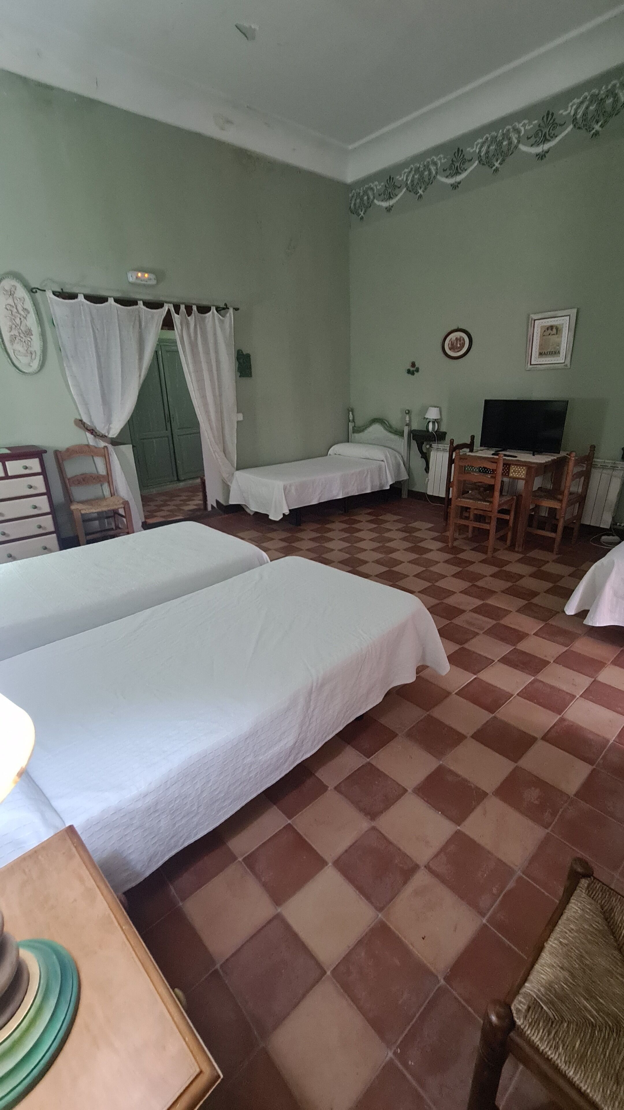 Quarto com duas camas, uma escrivaninha, uma cadeira, uma televisão e piso estampado.