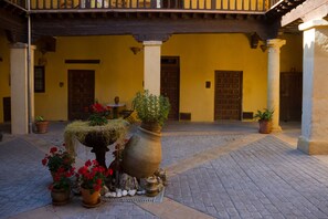 A courtyard with a tiled floor, potted plants, and a large urn. - Casa Palacio Conde de Garcinarro (Huete)