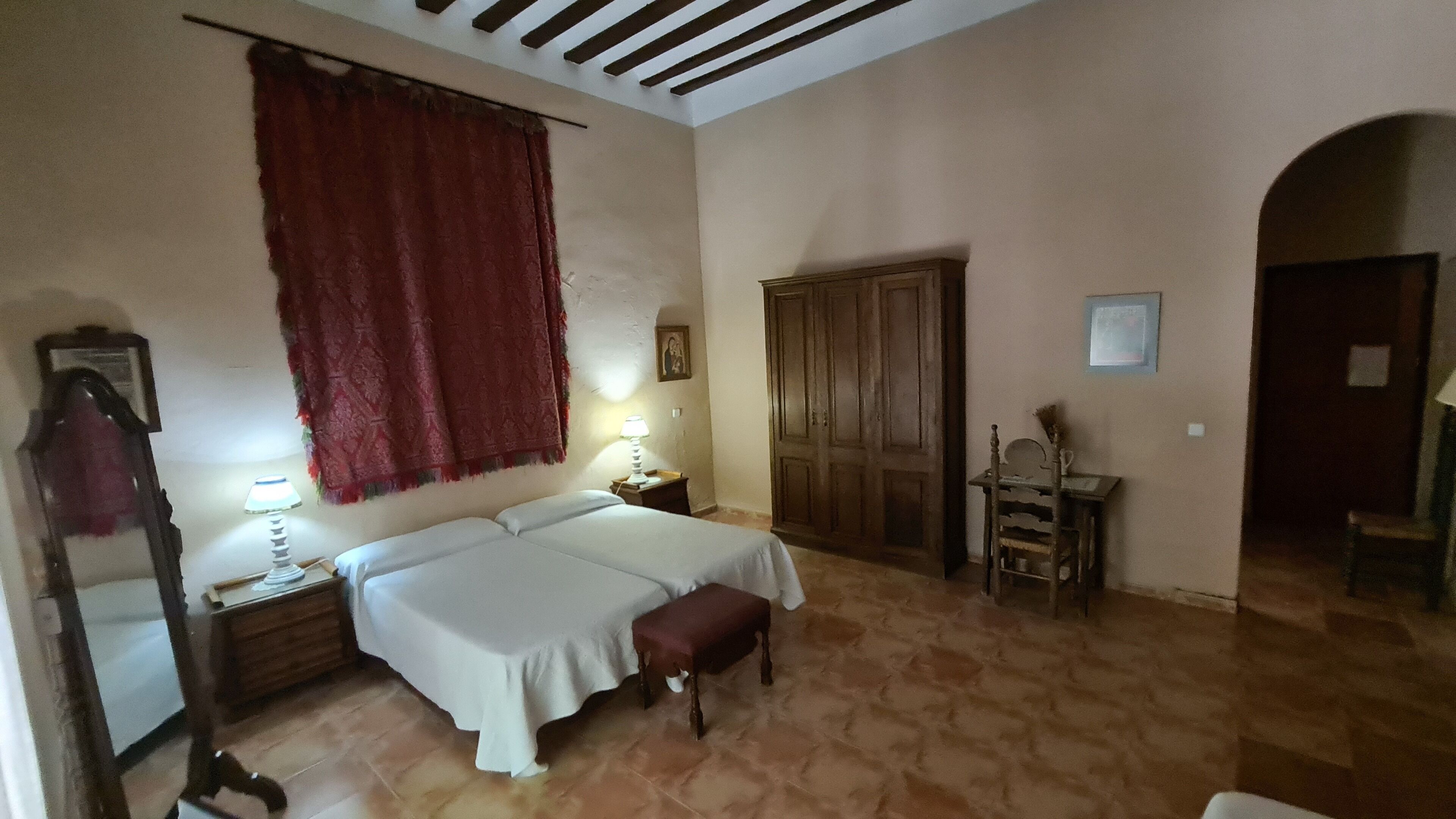 Una habitación con dos camas, un armario de madera, un escritorio con silla y un espejo.