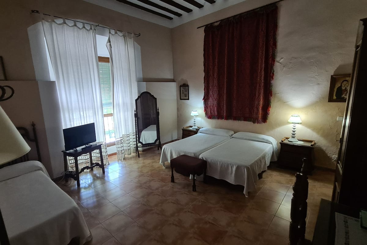 A bedroom with a bed, a desk with a TV, a chair, and a window with curtains.