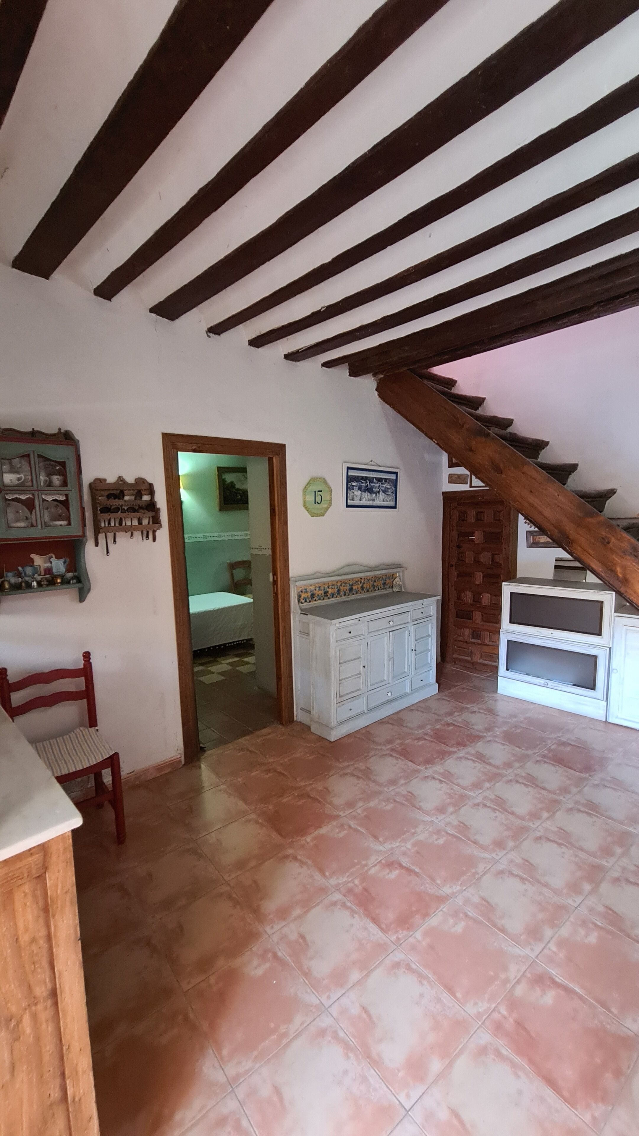 A room with a sloped ceiling, a tiled floor, a wooden chair, a cabinet, and a door leading to another room.