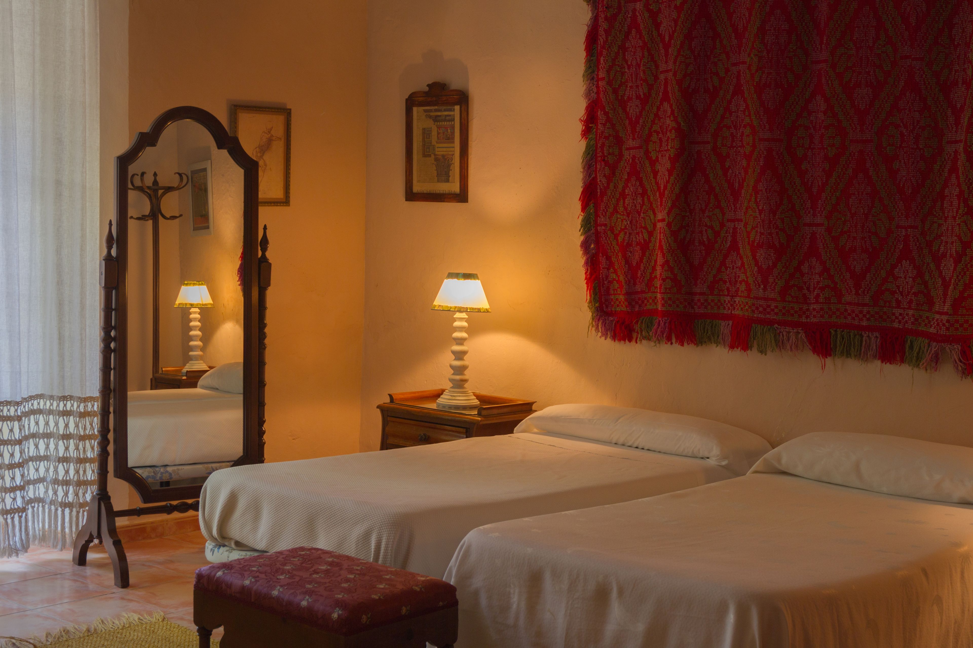 A bedroom with two beds, a nightstand, a mirror, and a red patterned wall hanging.