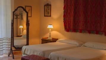 A bedroom with two beds, a nightstand, a mirror, and a red patterned wall hanging.