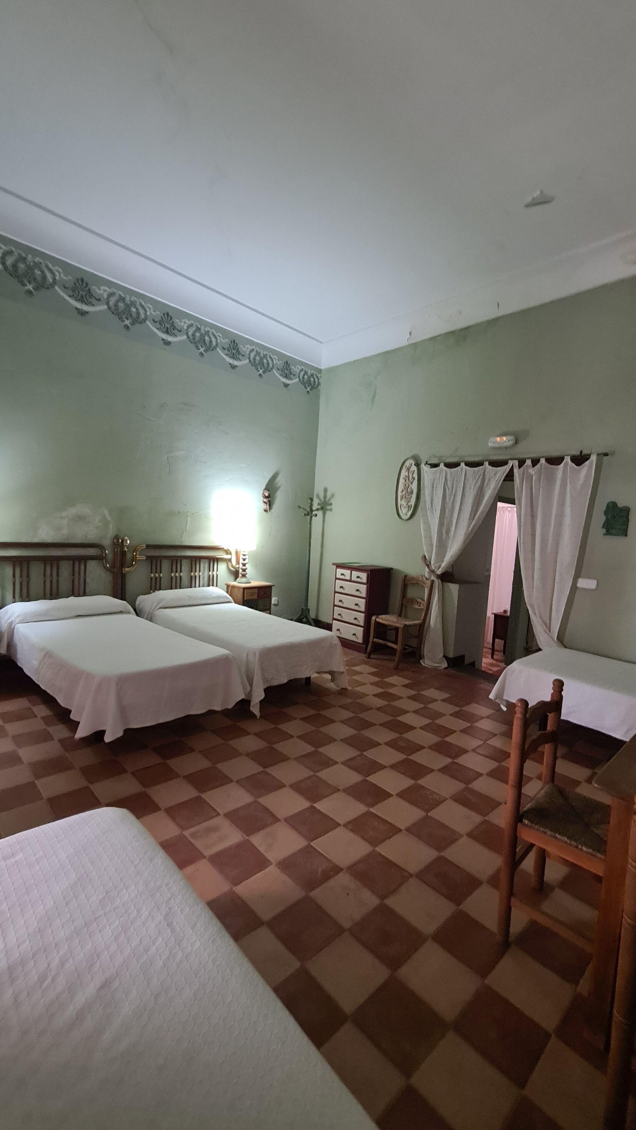 Una habitación con dos camas, una silla de madera, un aparador y piso a cuadros.