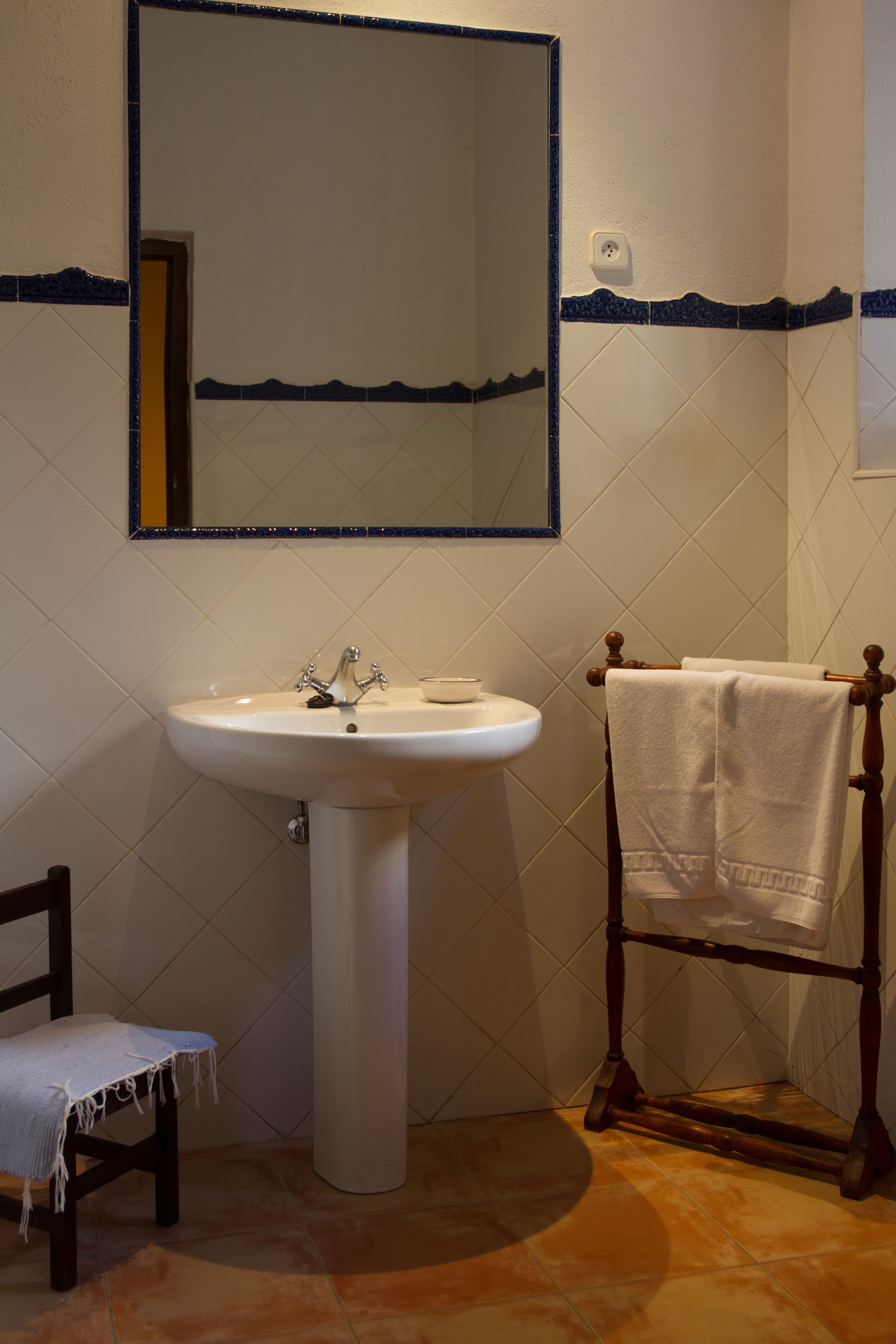 Une salle de bain avec un lavabo blanc, une chaise en bois et un porte-serviettes.