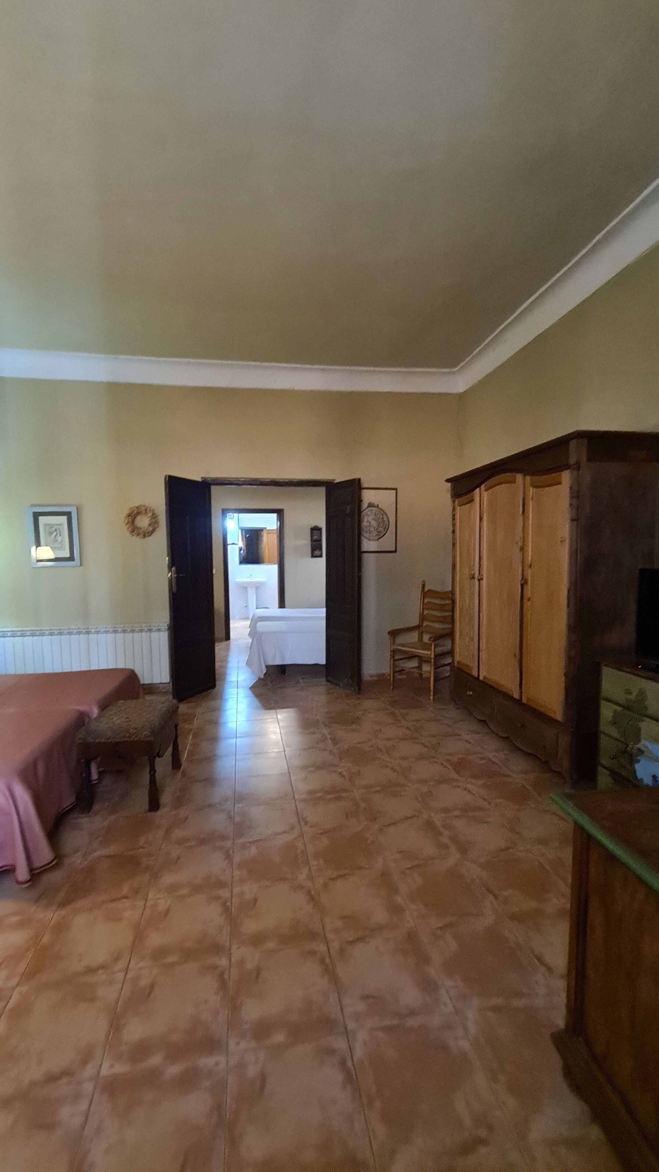 Una habitación con una cama, un armario de madera, una silla y una puerta que da a otra habitación.