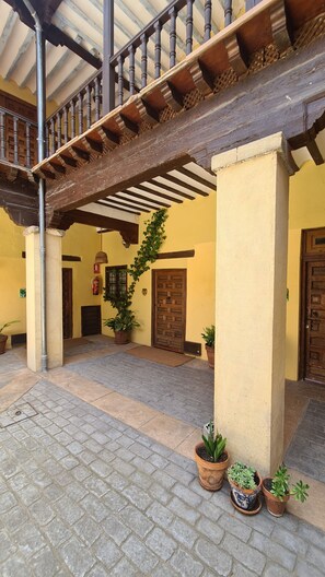 A covered courtyard with a wooden balcony, potted plants, and a traditional wooden door. - Casa Palacio Conde de Garcinarro (Huete)