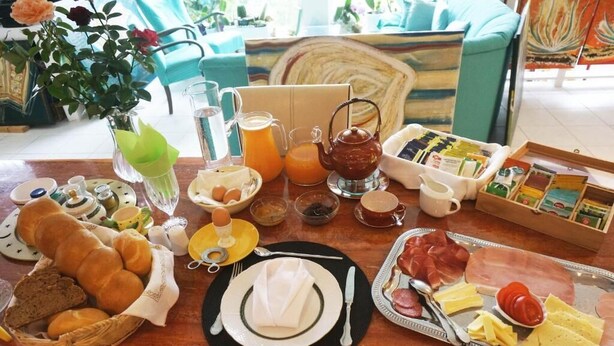 Una mesa de madera con una bandeja de desayuno que incluye pan, huevos, queso, jamón y jugo.