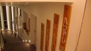 Un pasillo con una escalera que sube a una plataforma, flanqueado por arte de madera en las paredes y un perchero.