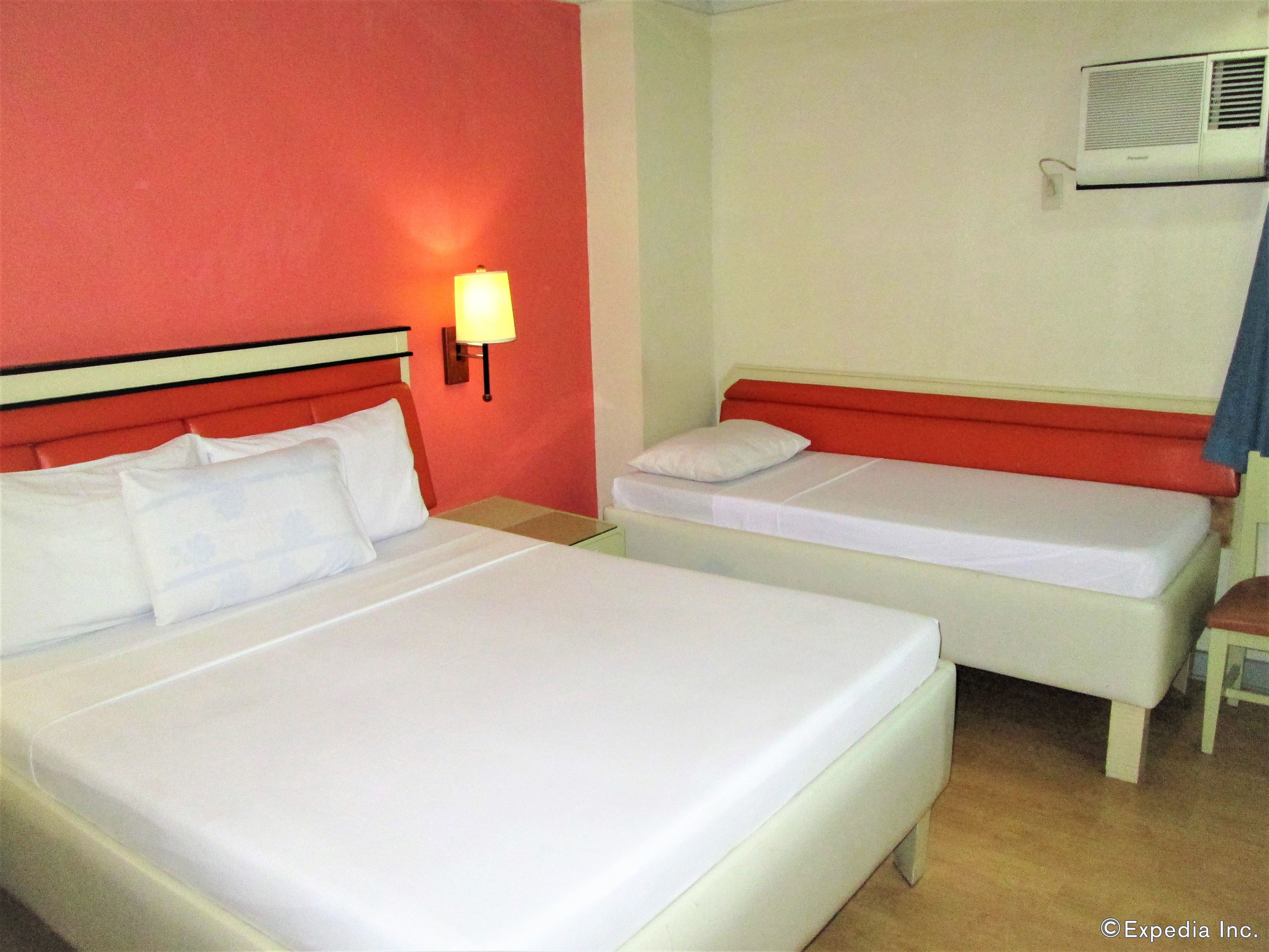 Habitación de hotel con dos camas, una mesita de noche, una lámpara y un equipo de aire acondicionado.