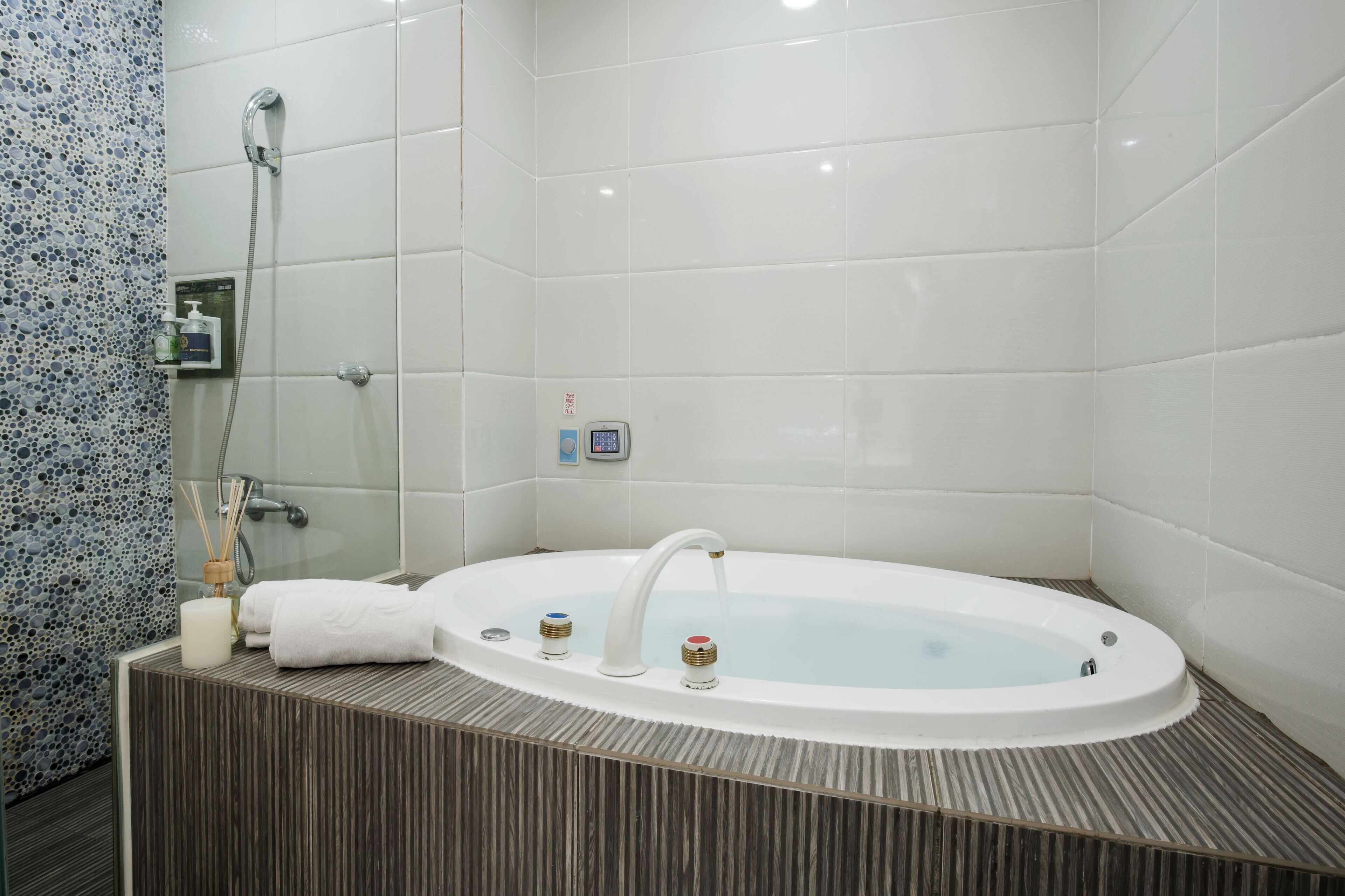 Een moderne badkamer met een vrijstaand bad, een handdouche en een bedieningspaneel aan de muur.